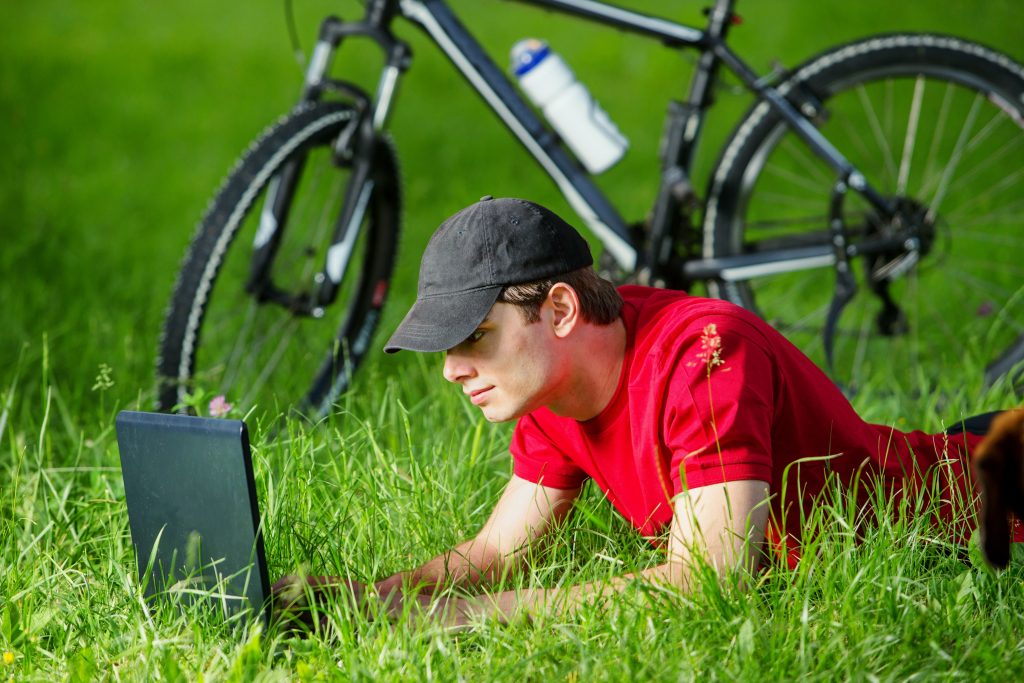 white man browsing online using computer on grasslands with bicycle on the side